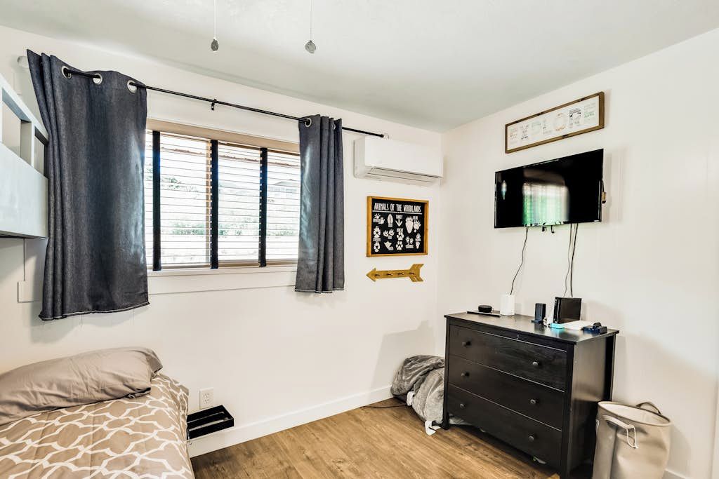 A bedroom with a bed, a dresser, a television, and a window with curtains.