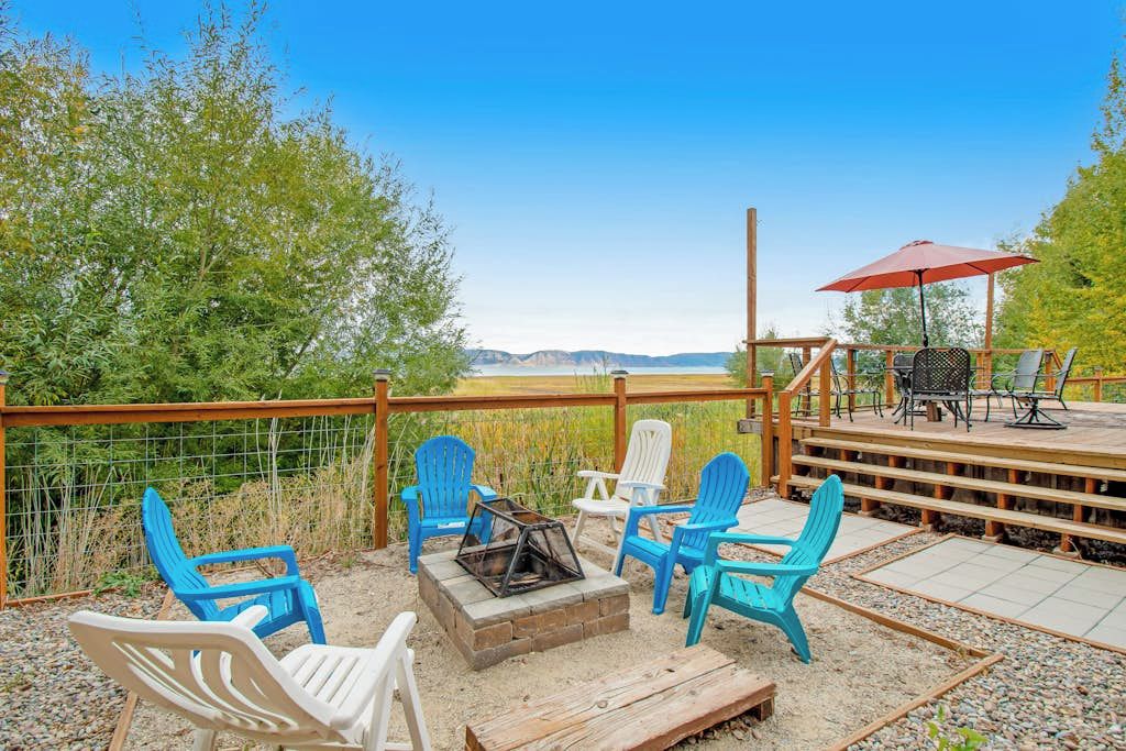 Un espacio al aire libre con sillas Adirondack, un brasero y vistas a un lago.