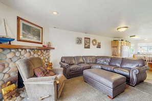 A living room with a stone fireplace, a large leather sectional sofa, and a grey armchair. - Tennis Court Condo - Lake Views, Pool & Hot Tub (Garden City)