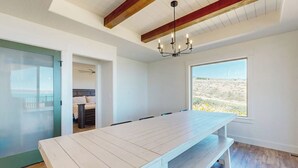 Een ruime kamer met een grote houten tafel, een kroonluchter en uitzicht op een woestijnlandschap.