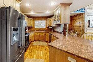 A kitchen with wooden cabinets, a stainless steel refrigerator, and a granite countertop. - Joining Families at Bear Lake (Garden City)