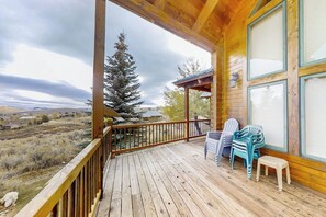 A wooden deck with a view of a mountainous landscape, a covered area with chairs, and a small table. - Joining Families at Bear Lake (Garden City)