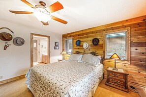 Ein Schlafzimmer mit Bett, Deckenventilator, Holzwänden, Nachttisch und an der Wand befestigten Hüten.
