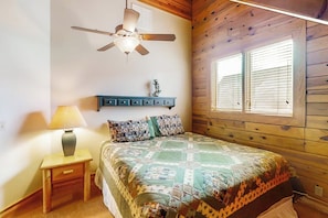 A bedroom with a wooden ceiling, a bed with a quilt, a nightstand with a lamp, a ceiling fan, and a window with blinds. - Joining Families at Bear Lake (Garden City)