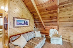 Ein Holzinnenraum mit einer Couch und einem Sessel, einem gerahmten Bild an der Wand und einer schrägen Decke.