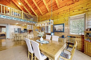 Ein geräumiger Essbereich mit Holztisch und -stühlen, eine Küche im Hintergrund und ein Balkon mit Geländer.