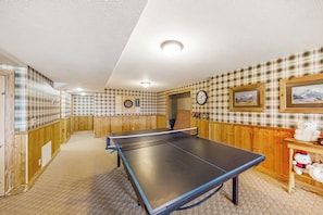A room with a ping pong table, wooden walls, a clock, and a framed picture. - Joining Families at Bear Lake (Garden City)