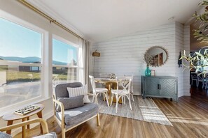 A room with a large window, a dining table, chairs, a sofa, a small table, and a cabinet. - Secluded Sunrise - Lake Views, Sleeps 23, Dogs OK (Garden City)