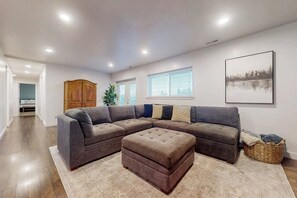 A living room with a sectional sofa, ottoman, and a large painting on the wall. - Secluded Sunrise - Lake Views, Sleeps 23, Dogs OK (Garden City)