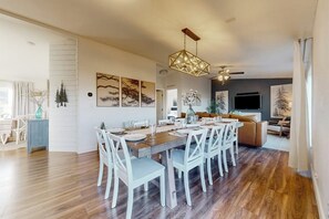 A dining area with a long wooden table, white chairs, and a hanging light fixture. - Secluded Sunrise - Lake Views, Sleeps 23, Dogs OK (Garden City)