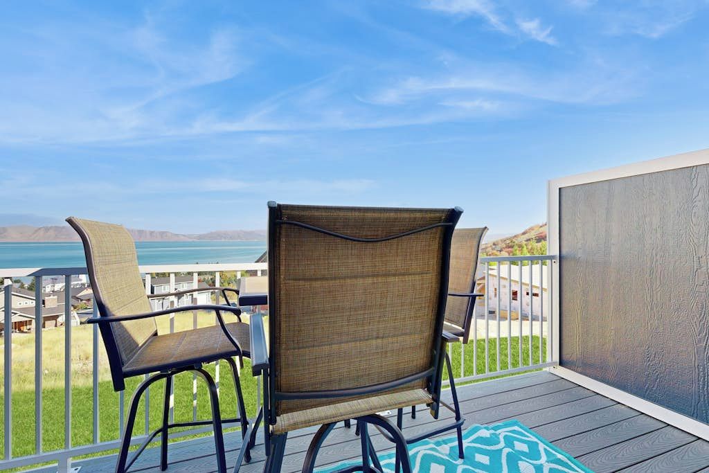 A balcony with two wicker chairs and a table, overlooking a body of water and distant hills.
