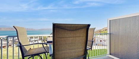 A balcony with two wicker chairs and a table, overlooking a body of water and distant hills.