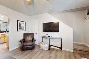 A living room with a brown leather chair, a small table, a television mounted on the wall, and a door. - Bear Lake Blue - Lake Views, Heated Pool, Hot Tub (Garden City)