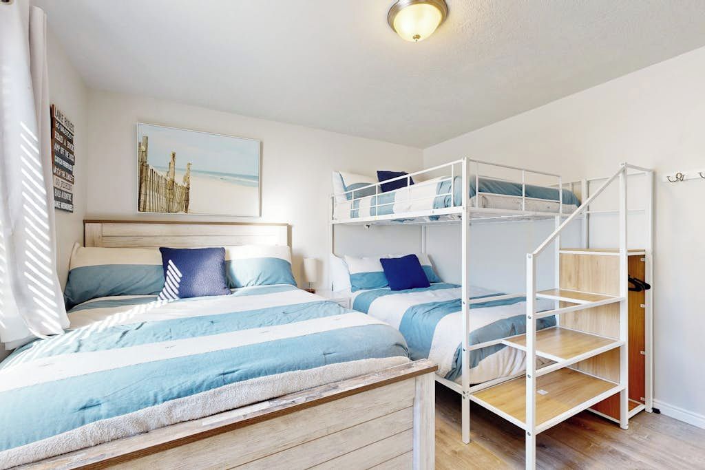 Una habitación con literas, un banco de madera, una cama con ropa de cama a rayas, un estante en la pared y un cuadro enmarcado.