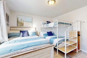 Een kamer met stapelbedden, een houten bank, een bed met gestreepte lakens, een wandplank en een lijst met een afbeelding.