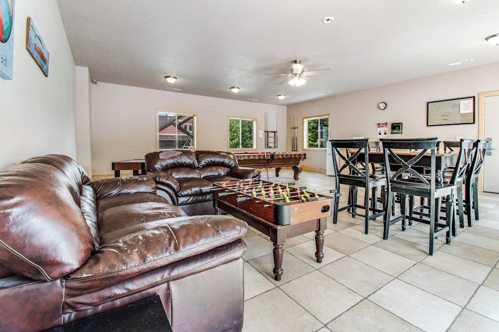 A living room with a leather sofa, a foosball table, and a dining area with chairs and a table.