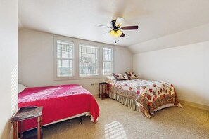 Ein Schlafzimmer mit zwei Betten, einem Deckenventilator und großen Fenstern.