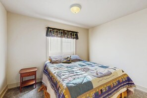 Une chambre à coucher avec un lit, une table de chevet, une fenêtre avec des stores et un luminaire au plafond.