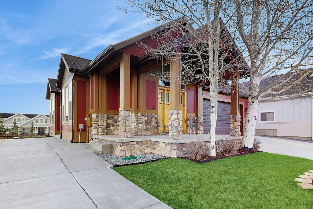 A two-story house with a stone foundation, a red and yellow facade, and a front porch with a tree.