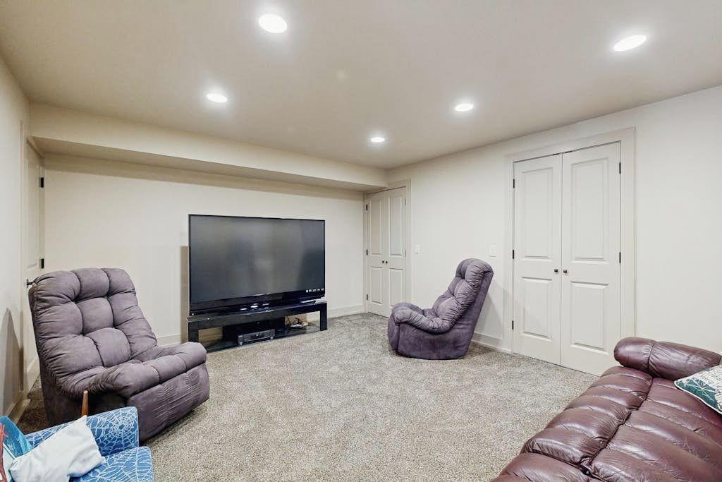 A living room with a flat-screen TV, two recliner chairs, a brown sofa, and a white door.