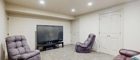 A living room with a flat-screen TV, two recliner chairs, a brown sofa, and a white door.