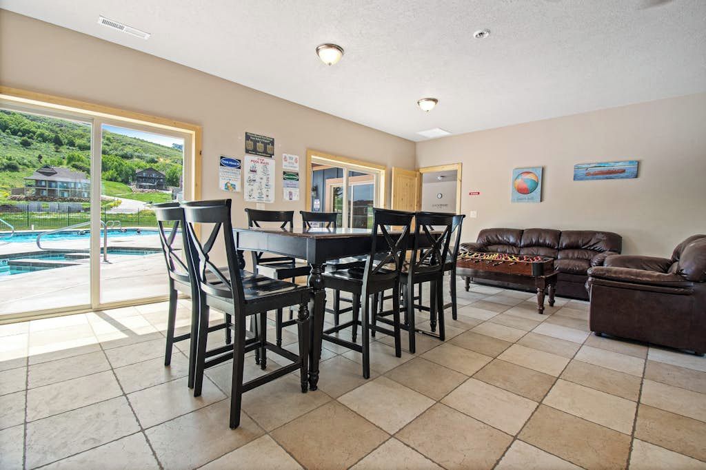 A spacious living area with a dining table and chairs, a leather sofa, and a view of a swimming pool.