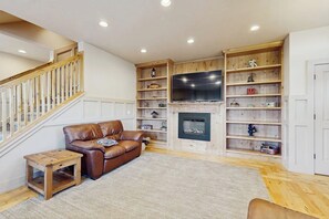 Un salon avec un escalier, un canapé en cuir, des étagères en bois, un téléviseur à écran plat et une cheminée.