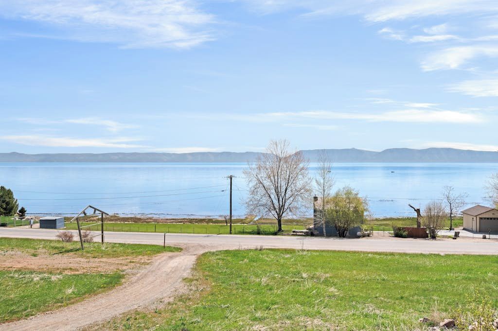 A rural landscape with a clear view of a lake, a dirt path, and a small building.