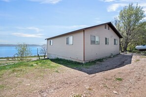 A single-story house with a sloped roof, positioned on a dirt ground with a grassy area in front. - Meadow Mountain Home (Garden City)