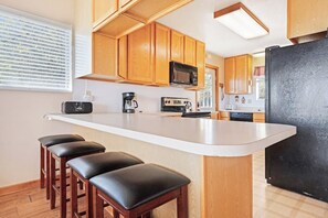A kitchen with wooden cabinets, a black refrigerator, a microwave, and a coffee maker. - Meadow Mountain Home (Garden City)
