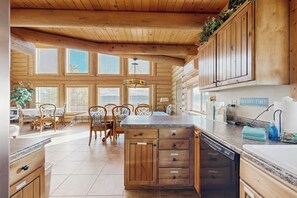 A log cabin interior with a kitchen featuring wooden cabinets, a central island, and a dining area with chairs and a table. - Elk Ridge Lodge - Log Cabin with Lake Views (Garden City)
