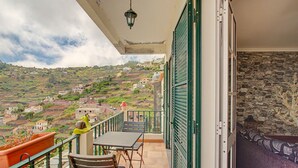 A balcony with a table and chairs, overlooking a hillside village. - Holiday Home 'Vista Atlântica Garachico' with Sea View, Private Terrace & Wi-Fi (Câmara de Lobos)