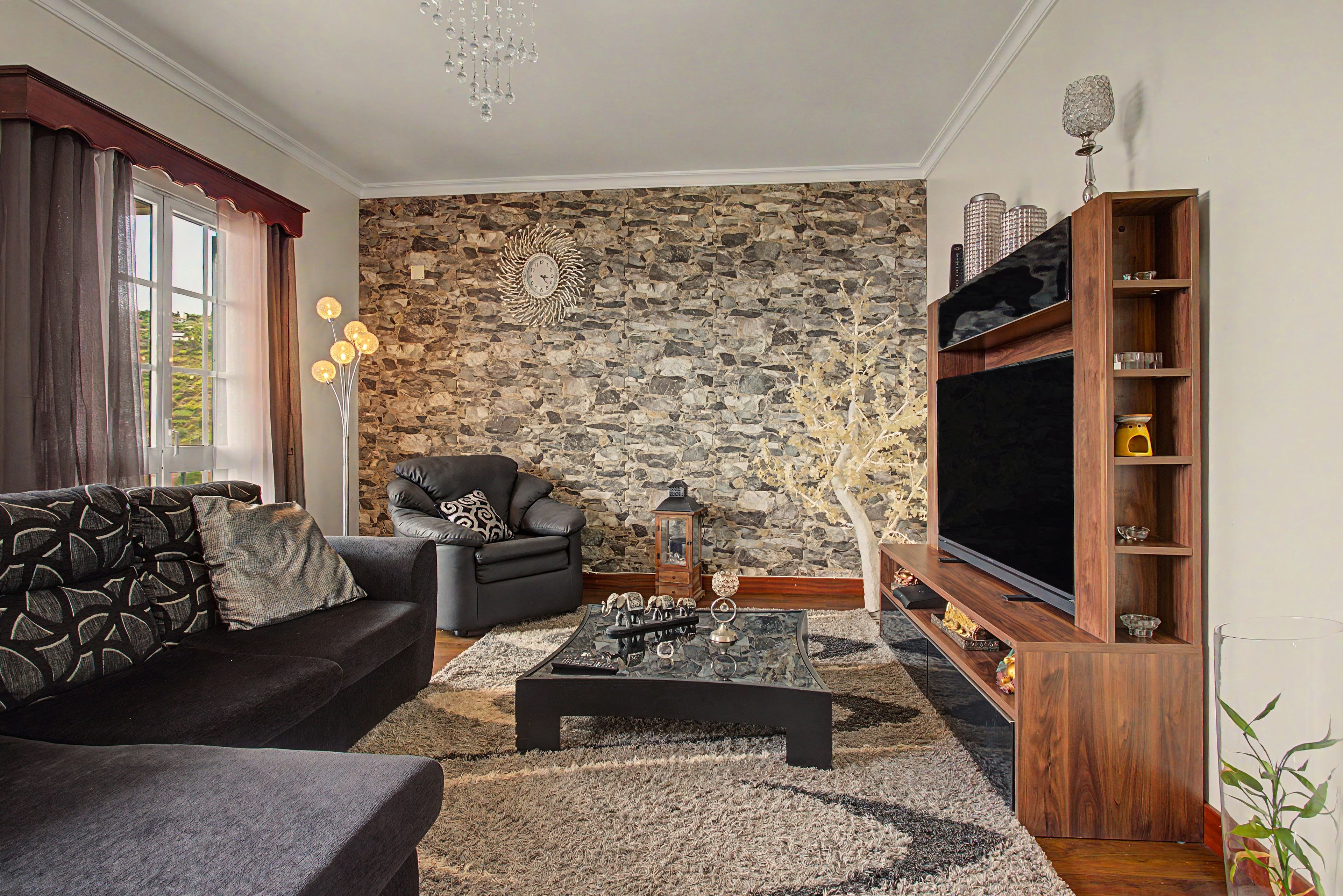 A living room with a stone wall, a sofa, a chair, a coffee table, and a TV stand.
