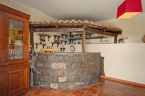 Una zona de bar con mostrador de piedra, estanterías de madera con botellas y un armario de madera con puertas de cristal.