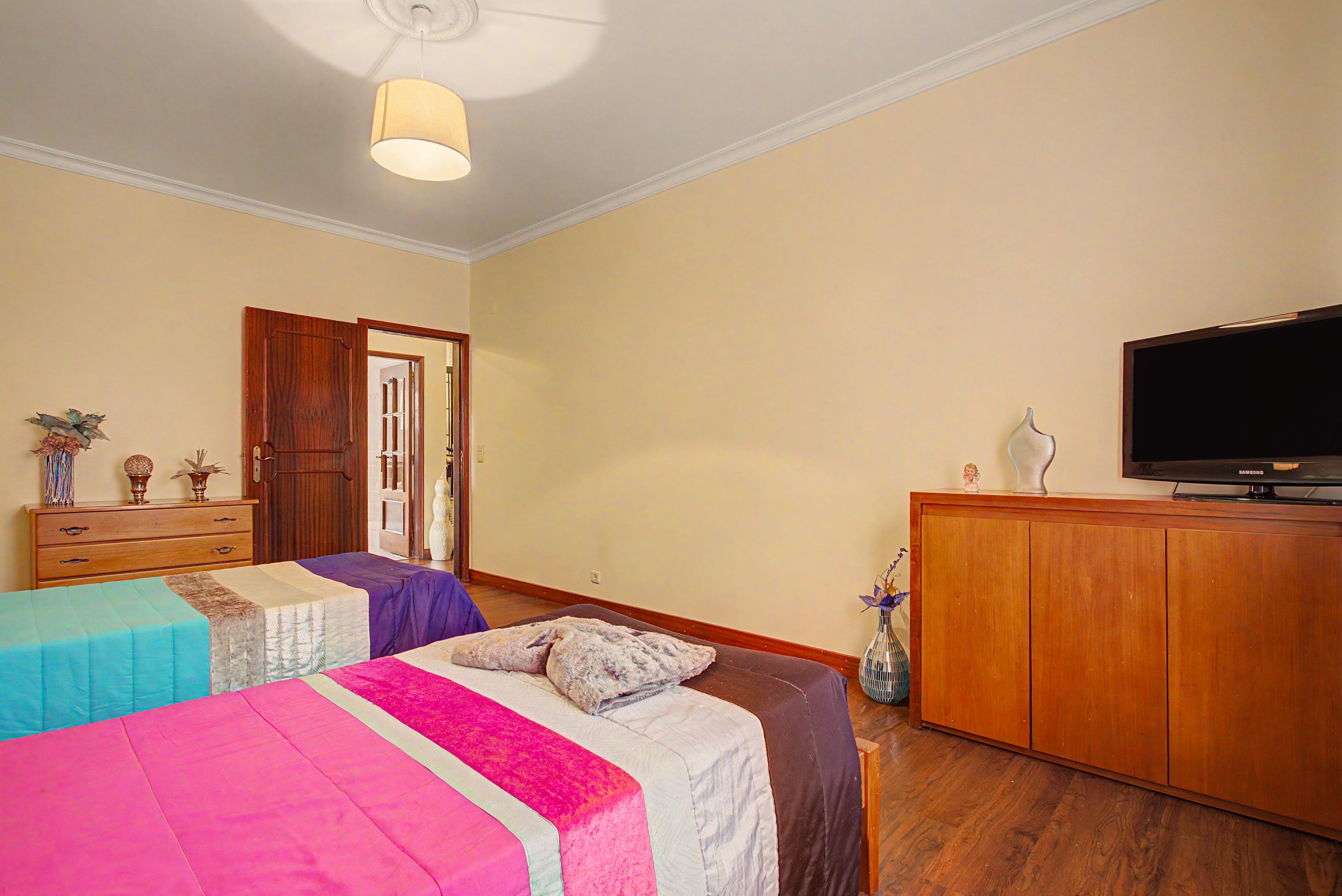 A hotel room with two beds, a television, a wooden cabinet, and a door leading to another room.