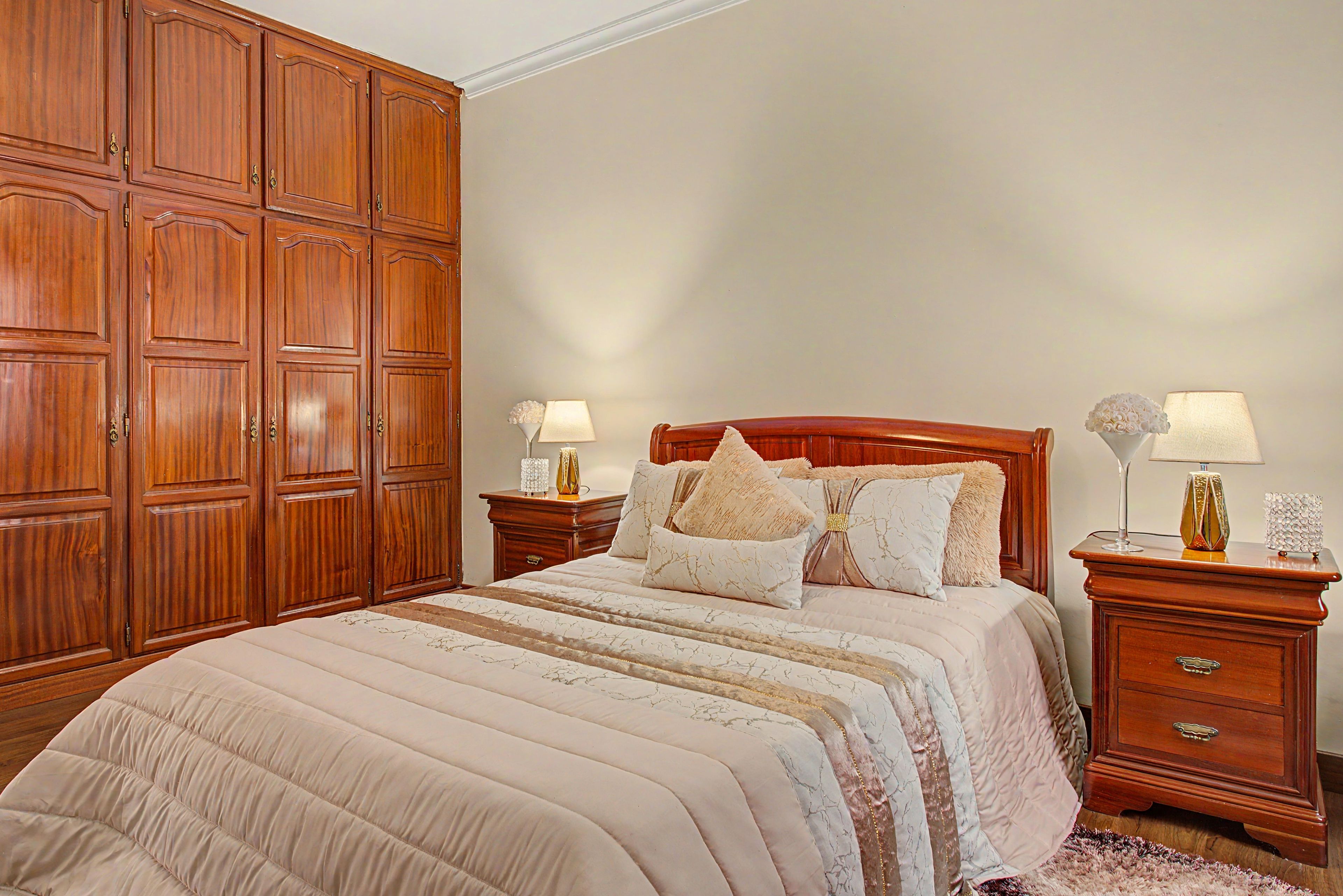 Une chambre à coucher avec une grande armoire en bois, un lit avec de nombreux oreillers et deux tables de chevet avec des lampes.