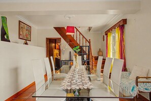 A dining area with a glass table, white chairs, and a staircase with wooden railings. - Holiday Home 'Vista Atlântica Garachico' with Sea View, Private Terrace & Wi-Fi (Câmara de Lobos)