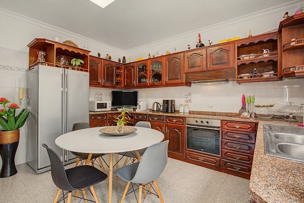 Una cocina con armarios de madera, un refrigerador, una mesa de comedor con sillas y un microondas.