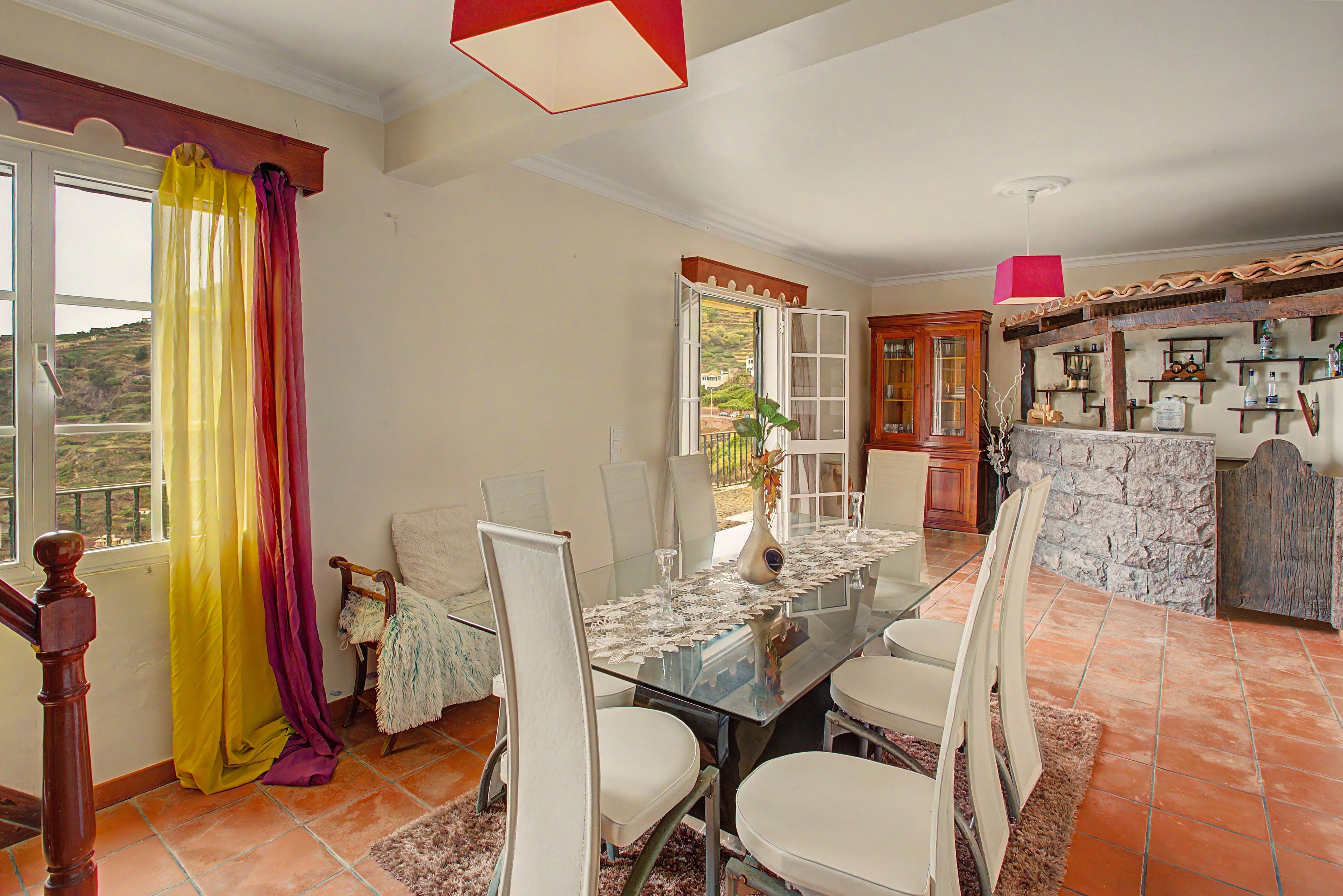 A dining area with a glass table, chairs, and a view through an open window.