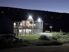 Ein zweistöckiges Haus mit einem Balkon, einem Basketballplatz und einer gut beleuchteten Auffahrt.