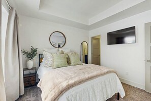 Ein Schlafzimmer mit einem Bett, einem Nachttisch, einem Spiegel, einem an der Wand montierten Fernseher und einer Tür.