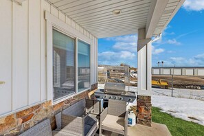 Eine überdachte Terrasse mit Grill, Korbmöbeln und Blick auf eine Baustelle.