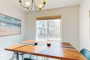 A dining area with a wooden table, chairs, a chandelier, a window with a view, and a framed picture on the wall. - Bear Lake Memories - Pickleball & Mountain Views (Garden City)