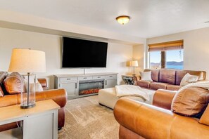 Een woonkamer met een flatscreen televisie, leren banken, een open haard en een raam met uitzicht.