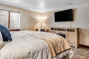 Een slaapkamer met een bed, een aan de muur bevestigde televisie, een nachtkastje en een lamp.