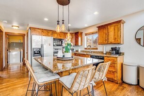 A kitchen with wooden cabinets, a granite countertop, and a central island with bar stools. - Peaceful Bear Lake Home (Garden City)