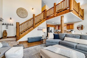 A living room with a wooden staircase, a sofa, a blue accent chair, and a dining area in the background. - Peaceful Bear Lake Home (Garden City)
