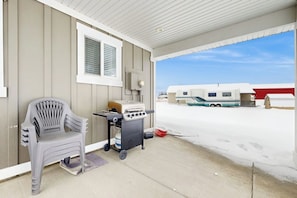 A covered porch with a grill, a chair, and a trailer in the background. - Shore Fun Cottage - ATV Access & Dog-Friendly (Garden City)