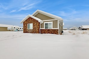 A single-story house with a stone facade and a gabled roof, surrounded by snow. - Shore Fun Cottage - ATV Access & Dog-Friendly (Garden City)