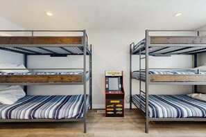 A room with bunk beds, a Pac-Man arcade machine, and a white ceiling. - Shore Fun Cottage - ATV Access & Dog-Friendly (Garden City)